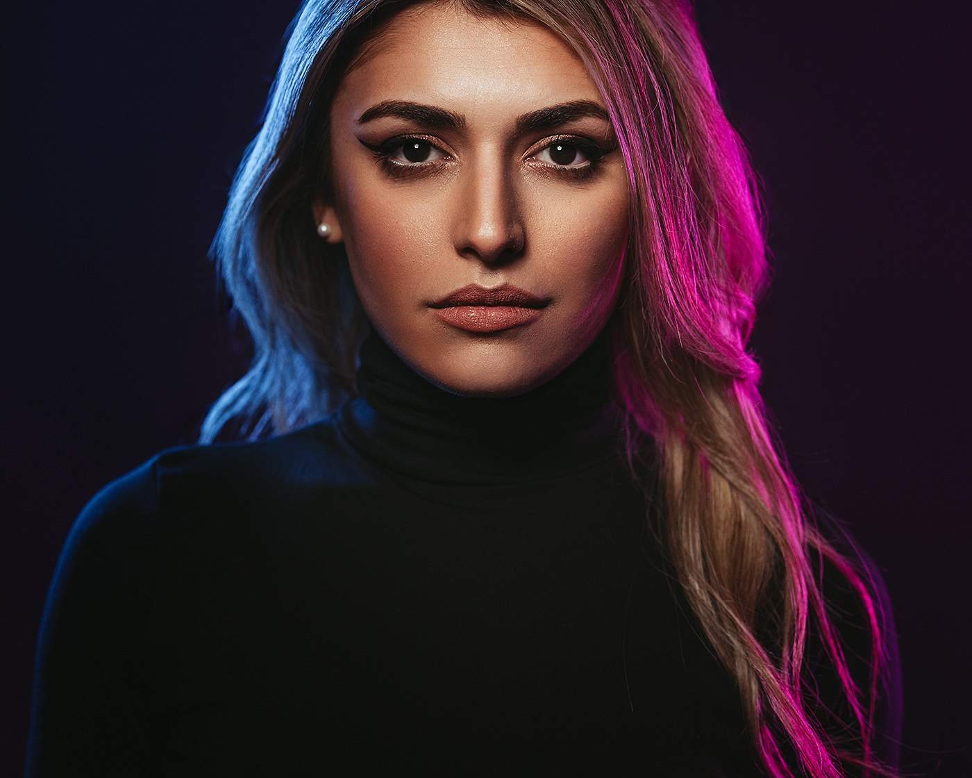 Portrait einer Frau im schwarzen Rollkragen mit blauem und pinkem Licht