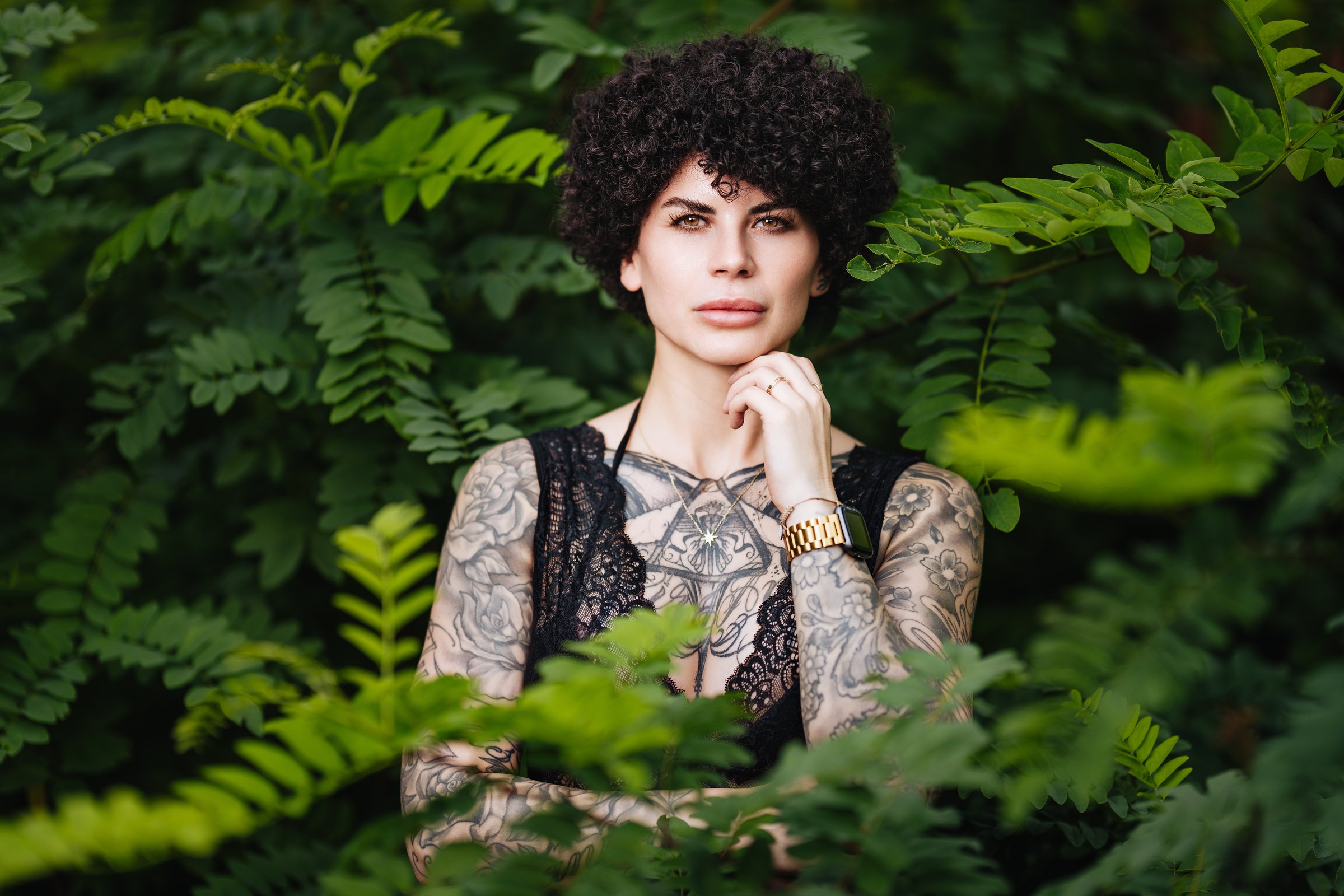 Tätowierte Frau mit Locken zwischen Farnblättern