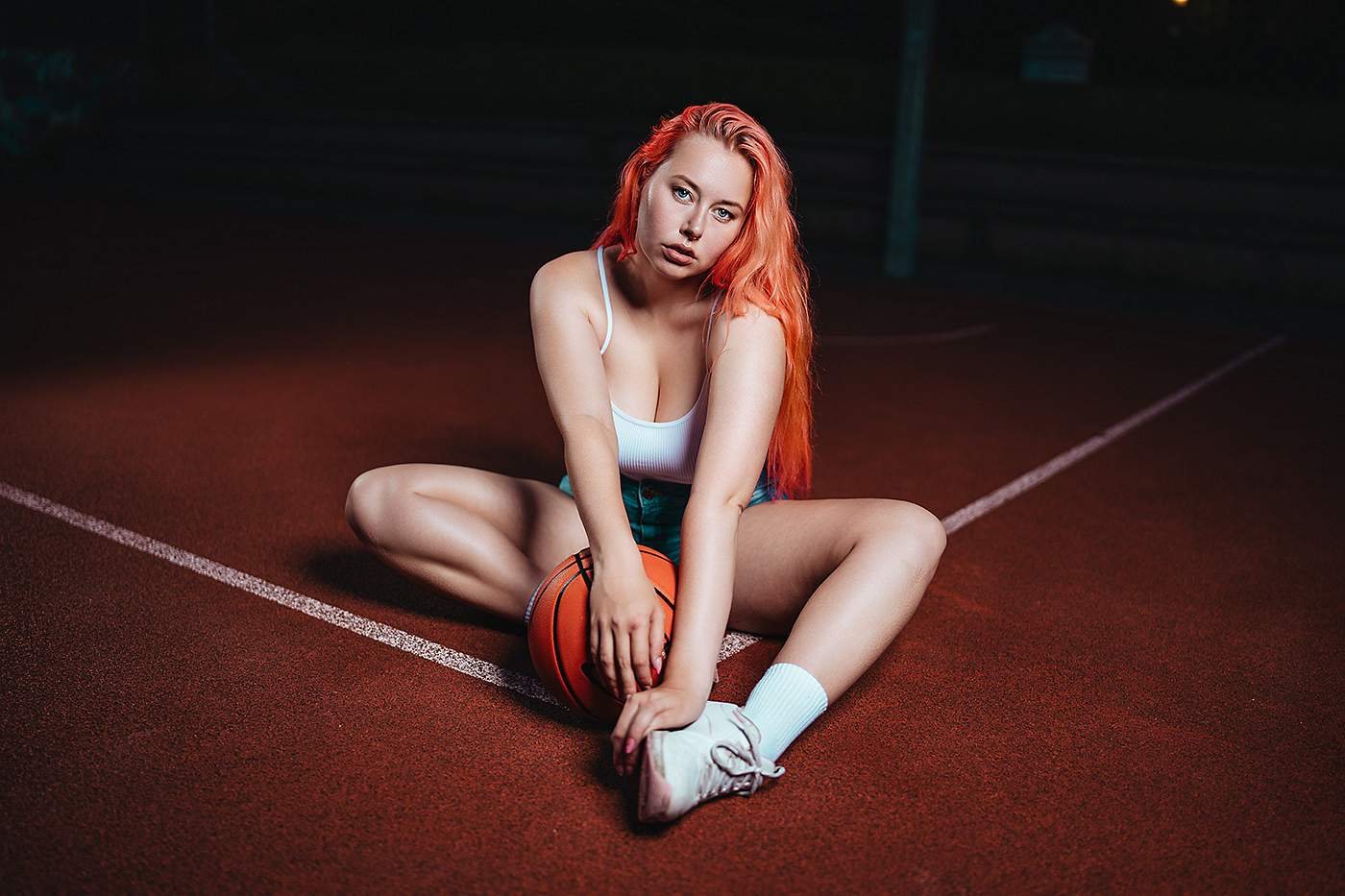 Frau mit roten Haaren sitzt mit Basketball auf dem Hallenboden